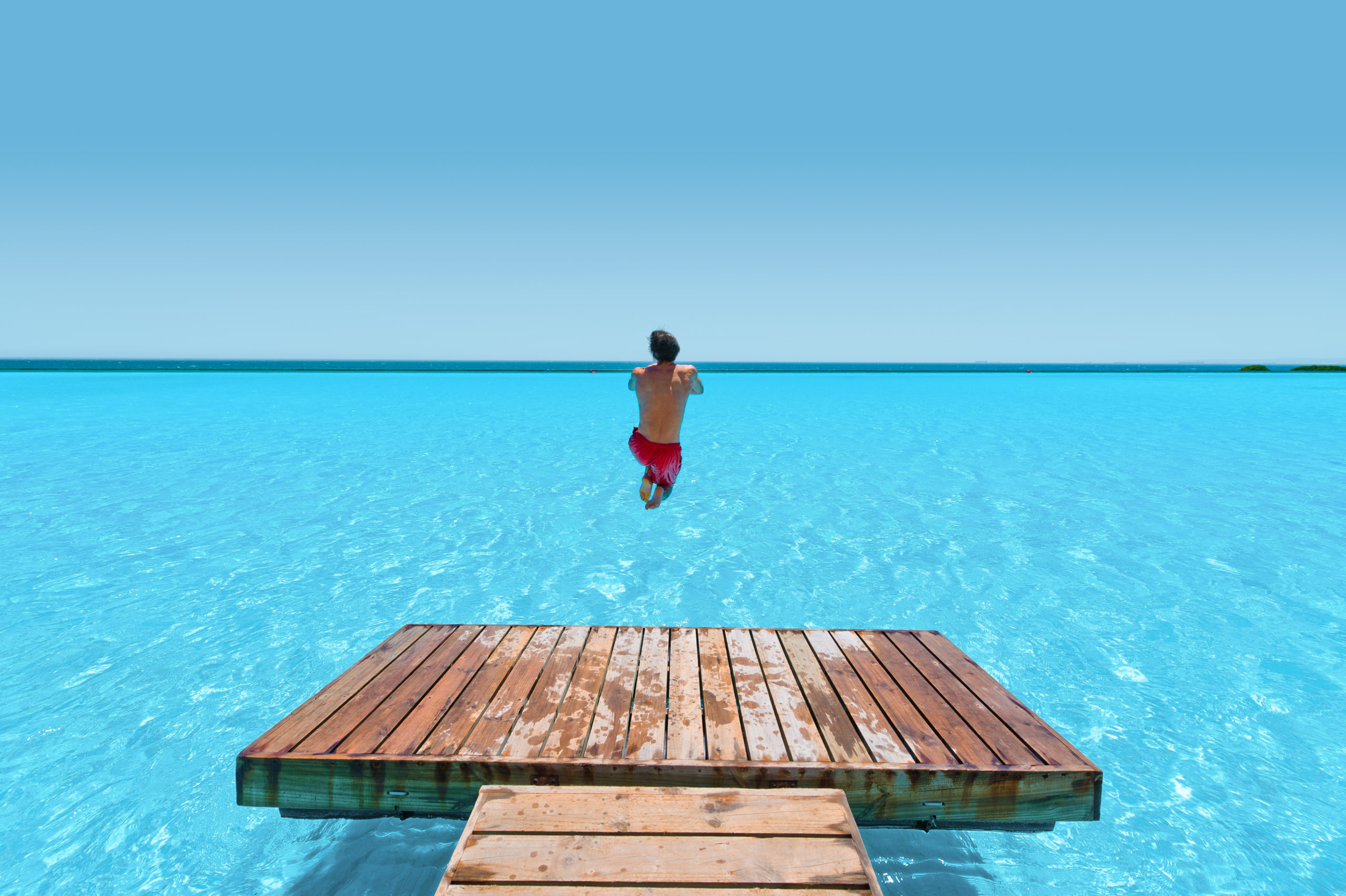 Man jumping into a large-scale pure turquoise lagoon powered by Crystal Lagoons