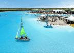 Aerial view of a large-scale turqoiuse lagoon in US, with a small sailing boat with a green sail and hundreds of people swimming