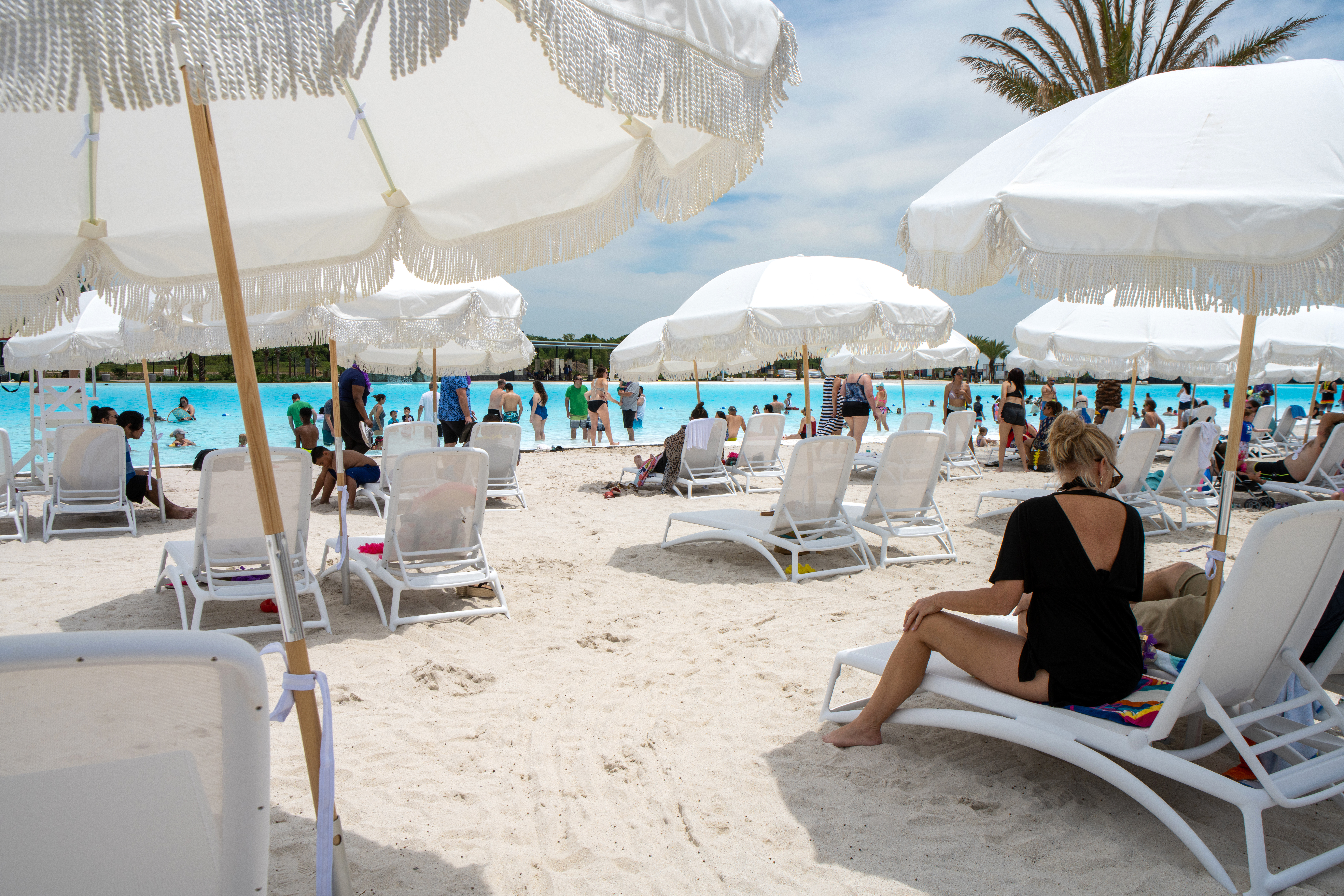 Sandy beach with lunge cahirs and white sun umbrellas overlooking a turquoise lagoon