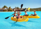 Young children play on two yellow kayaks on a turquoise lagoon