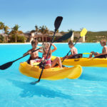 Young children play on two yellow kayaks on a turquoise lagoon