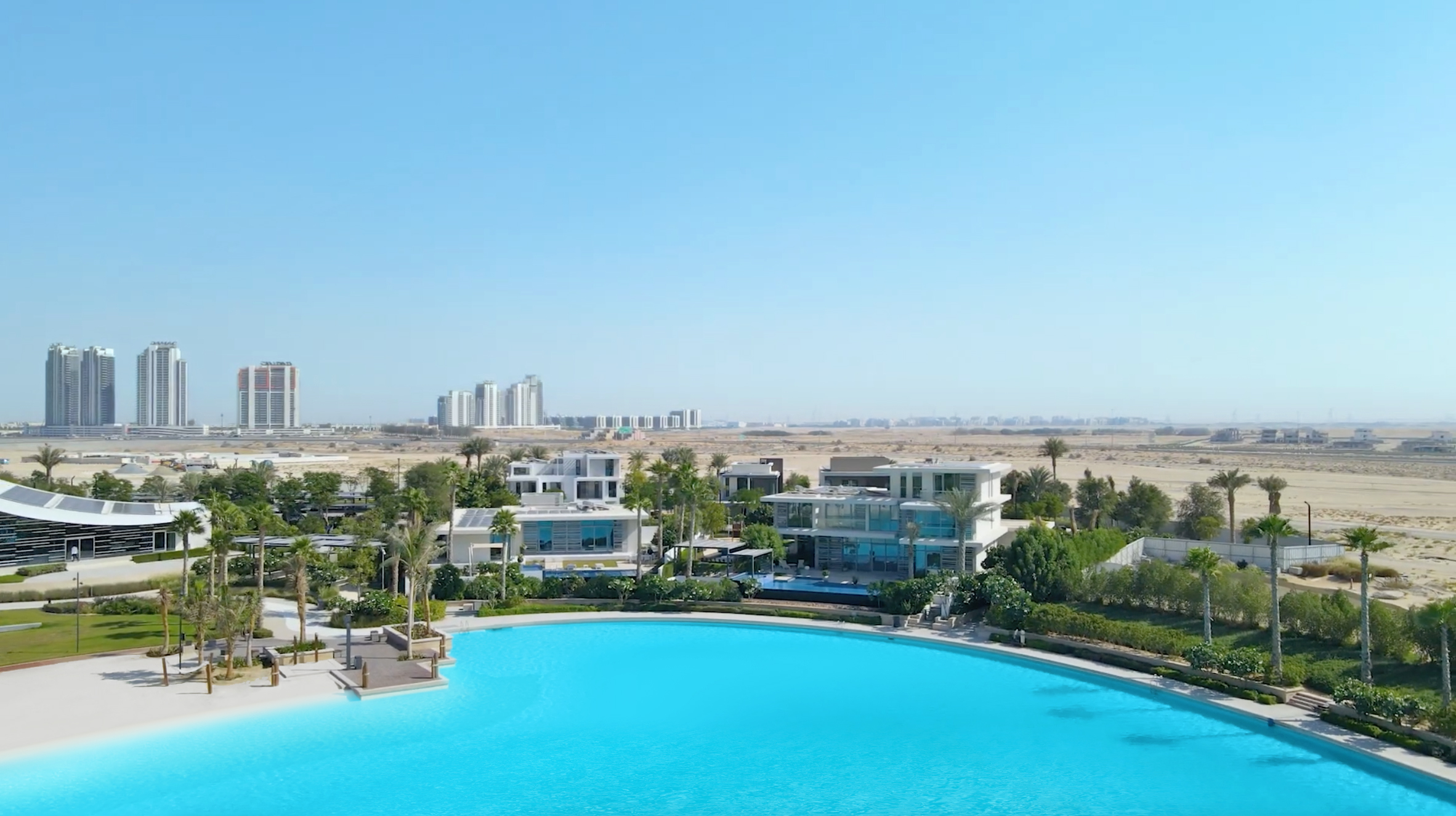 A turquoise lagoon surrounded by luxurious villas in the desert and skyscrapers in the background